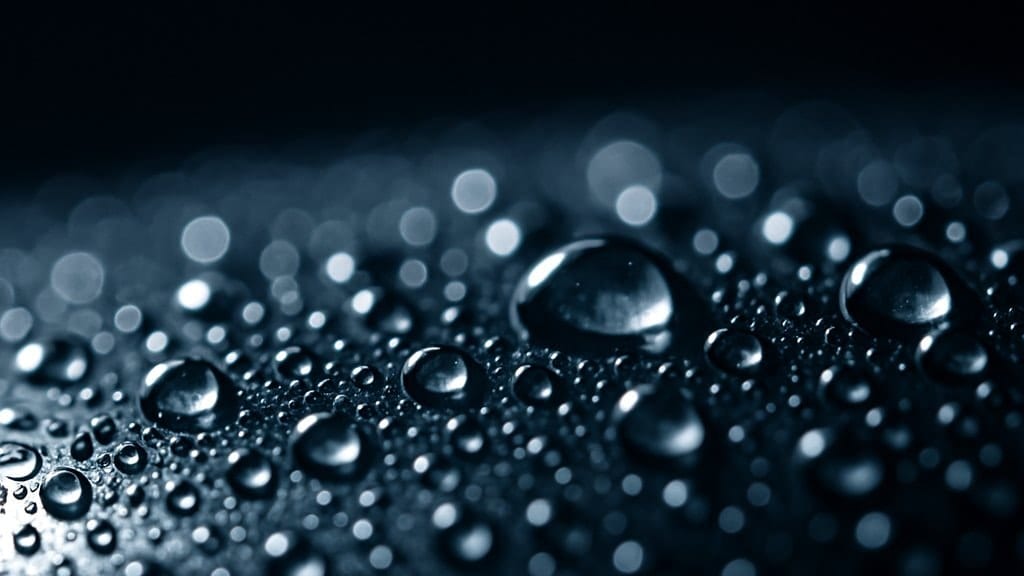 Editorial macro of condensation droplets forming on a cold polished stainless-steel surface, symbolising moisture behaviour
